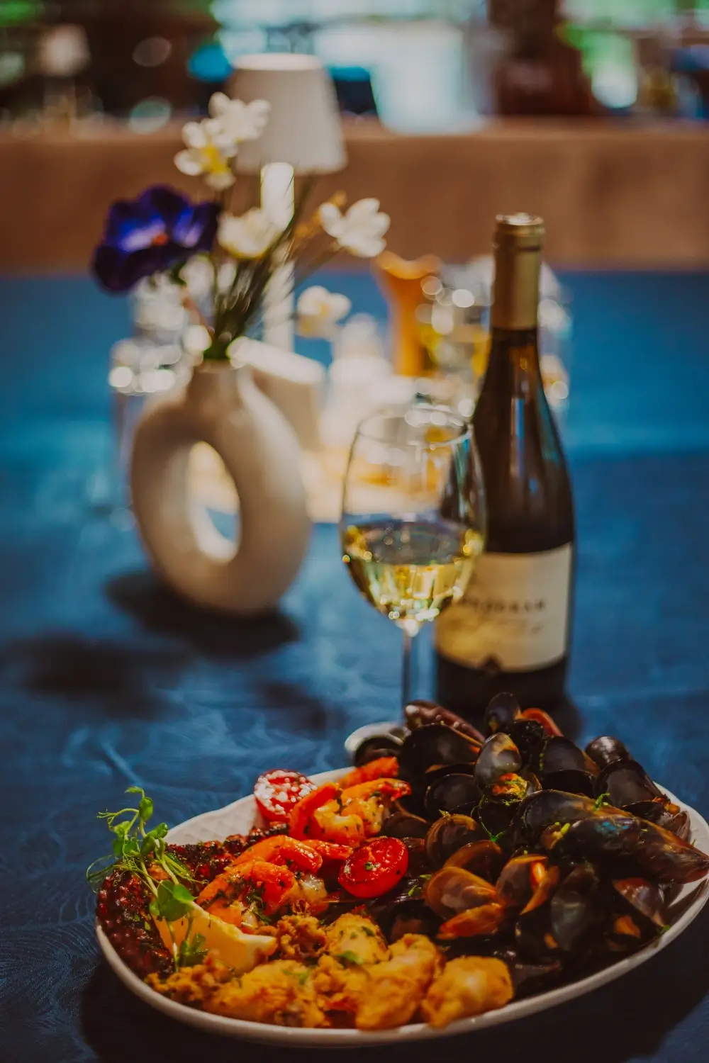 Platou cu fructe de mare, incluzând midii, creveți, caracatiță și calamar prăjit, servit cu un pahar de vin alb într-un decor elegant la Restaurant Dukova House